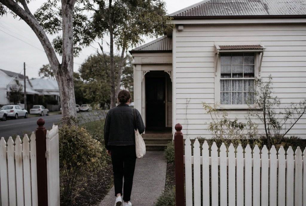A support worker walks up the front path of a weatherboard house on a quiet Melbourne street.