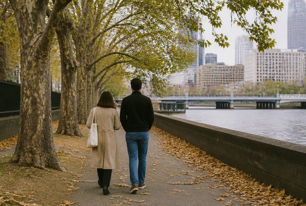 Two people walk side by side along the Yarra River path under autumn trees.